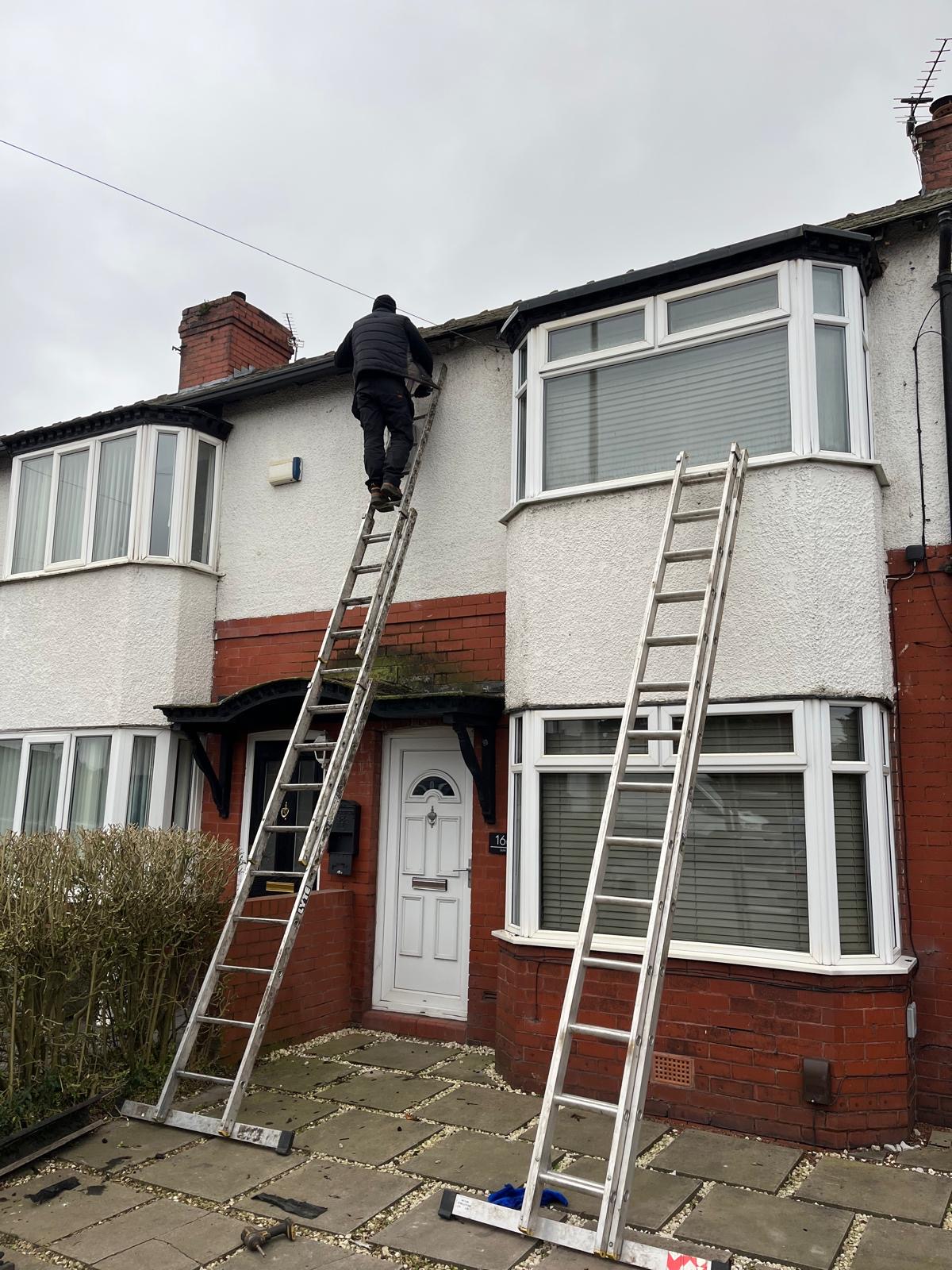 A worker on ladders at the roofline of a brick and rendered home